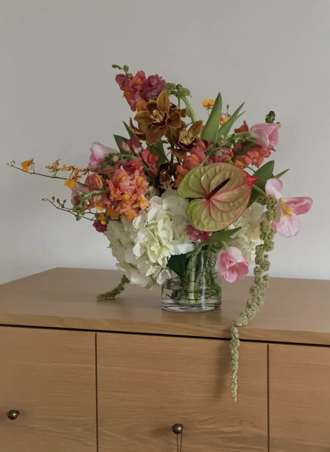 Bright arrangement with cymbidium orchid, snapdragon, anthurium and trailing amaranthus