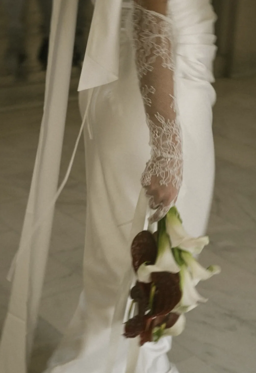 Detail of a white calla lily and burgundy anthurium bouquet held at the bride's side