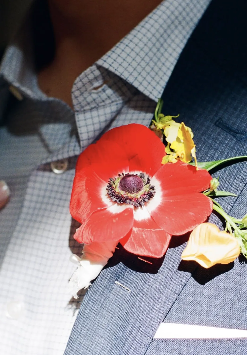 Red anemone boutonniere with yellow orchid on a checked blue lapel
