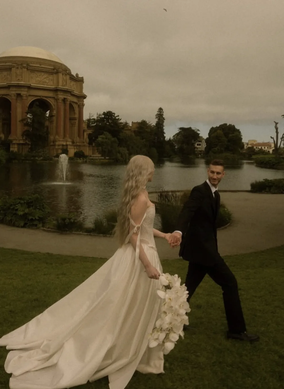 Couple walking the Palace of Fine Arts lawn with a white phalaenopsis cascade