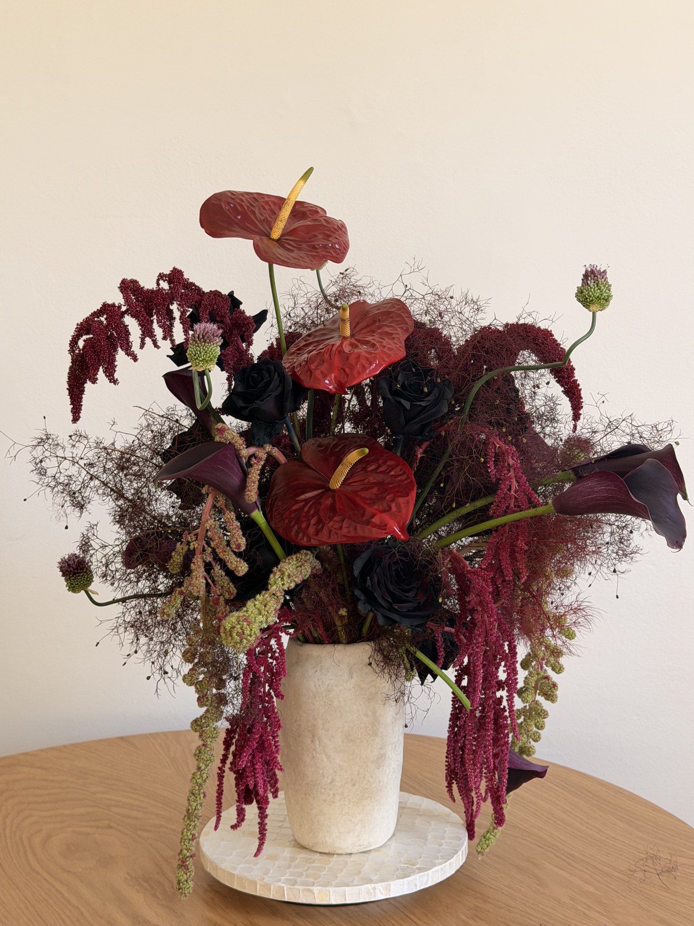 Large red anthurium and black rose arrangement with trailing amaranthus in a stone vase