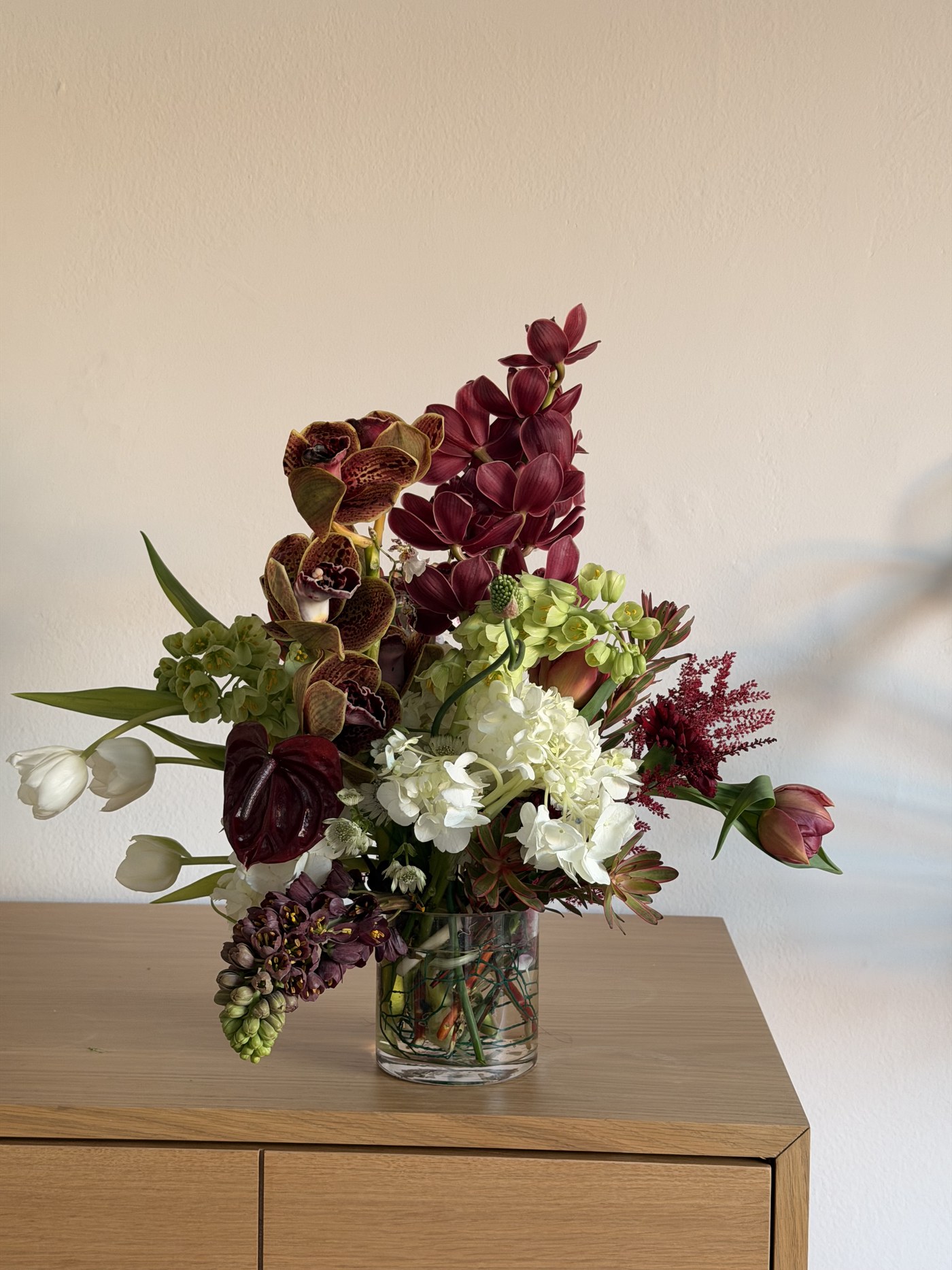 Medium burgundy arrangement with cymbidium orchid, white tulips and hydrangea
