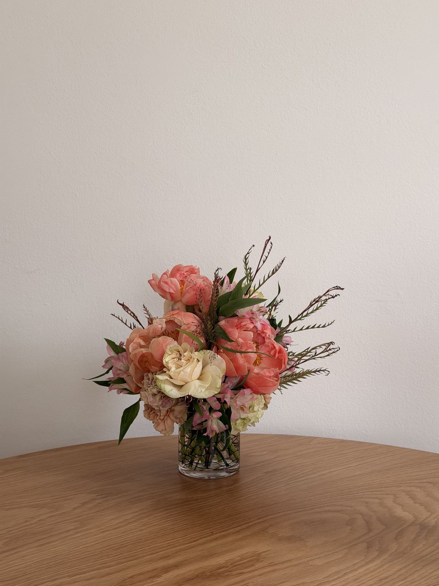 Small coral peony and garden rose arrangement in a glass vase
